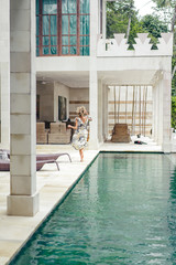 Obraz na płótnie Canvas back view of woman in beautiful dress running near swimming pool at villa