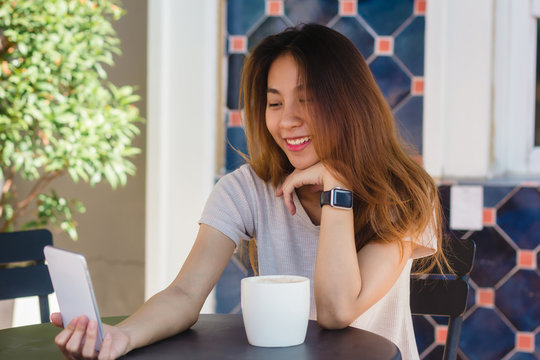 Attractive beautiful happy young Asian woman taking a selfie using a smart phone at cafe. Young Asian girl at restaurant taking self portrait.