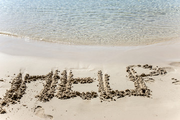 Text HELP etched in the sand on the seashore. Plea for help to survive. Request for support on the tropical coast.