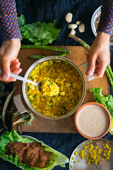 Woman hands tastes pot with cooked bulgur wheat grain porridge with turmeric powder, garlic and spices served for lunch or dinner. Traditional arabic, asian, middle east. Vegan vegetarian healthy food