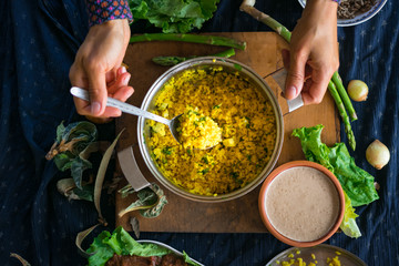 Woman hands tastes pot with cooked bulgur wheat grain porridge with turmeric powder, garlic and spices served for lunch or dinner. Traditional arabic, asian, middle east. Vegan vegetarian healthy food
