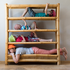 Young mother with three children in empty apartment was placed on shelves of bookcase. Kid and mom are happy together. Concept of compact housing.