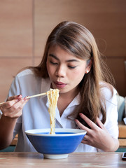 Close up happy asian woman using chopsticks for eating noodle at restaurant,lunch time concept.