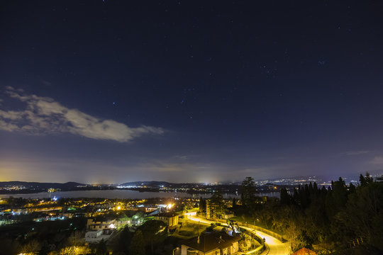 Time lapse of a panoramic view of a winter night sky with cloudy steps over cityscape with lake and hills.