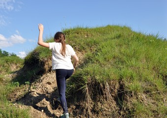 Fototapeta premium Child, blonde girl with long hair, climbing a little hill with green grass, backside