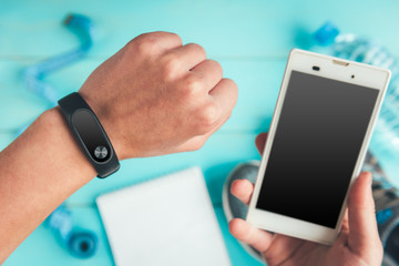 Fitness tracker on hand and mobile phone. Sneakers, bottle of water, tape measure on blue wooden background. Healthy lifestyle.