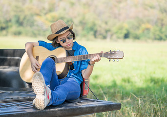 Woman wear hat and playing guitar on pickup truck