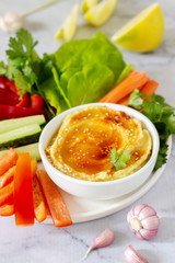 Hummus, different vegetables and lettuce leaves with lemon and garlic on a light background. Vegan food.