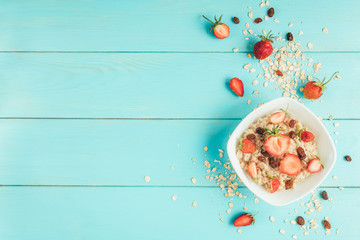 Oatmeal with fresh strawberry and raisins on blue wooden background. Healthy and diet food. Summer breakfast.
