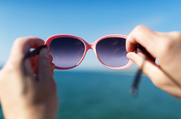 Soft focus on hand holding sunglasses over sea.