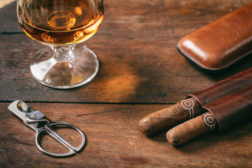 Cuban cigars closeup on wooden desk, blur glass of brandy