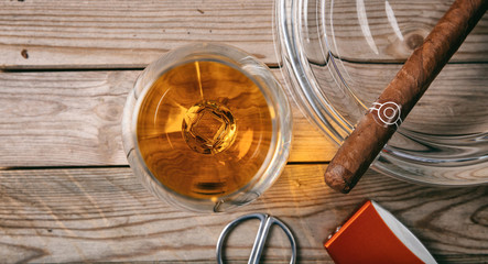 Cuban cigar and a glass of cognac brandy on wooden background, top view
