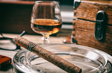 Cuban cigar closeup in an ashtray on wooden desk