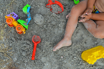 the child is playing with the sand. the kid sits on the gray sand and molds the figures. from tools at the small boy a shovel, an excavator, a plastic form for the lock and fish