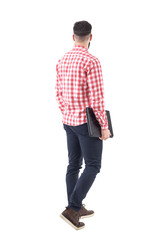 Rear view of young adult business man carrying laptop under arm walking and looking away. Full body...