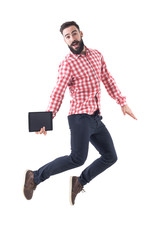 Successful excited young business man holding tablet jumping in mid air with open mouth. Full length isolated on white background. 