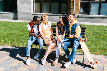 Fototapeta premium cheerful multicultural couples resting on bench together on street