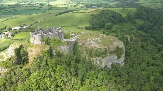 Aerial drone view of the ruins of a medieval castle located on a hilltop overlooking farmland (Carreg Cennen, Wales)