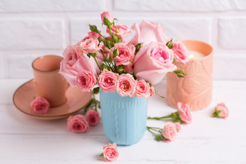 Pink roses flowers in blue cup, burning candle and little cup for coffee