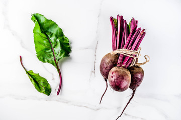 Fresh raw beetroot with green leaves, white marble background copy space top view