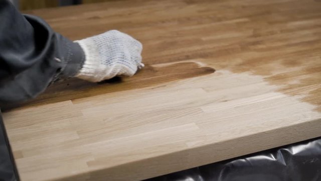 Professional carpenter is applying a layer of a oil on the sanded piece of wood.
