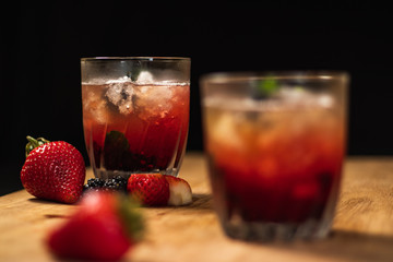 Bonito cóctel con zarzamoras, fresas y hojas de menta en un bonito vaso de vidrio sobre un fondo negro y de madera