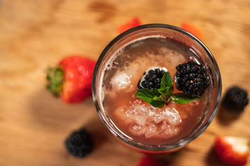 Bonito cóctel con zarzamoras, fresas y hojas de menta en un bonito vaso de vidrio sobre un fondo de madera