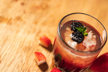 Bonito cóctel con zarzamoras, fresas y hojas de menta en un bonito vaso de vidrio sobre un fondo de madera