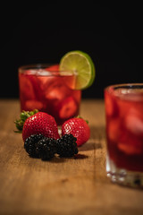 Bonito Cóctel con fresas, zarzamoras y una rodaja de limón para adornar en un fondo negro y de madera