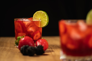 Bonito Cóctel con fresas, zarzamoras y una rodaja de limón para adornar en un fondo negro y de madera