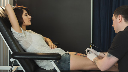 Professional tattoo artist making tattoo on leg