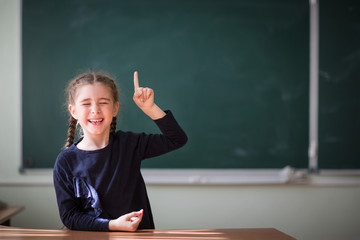 girl raised an index finger and laughing in front of a green school Board in school class