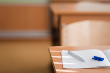 notebook and pen lying on the table close-up. School classroom in blur background without young student