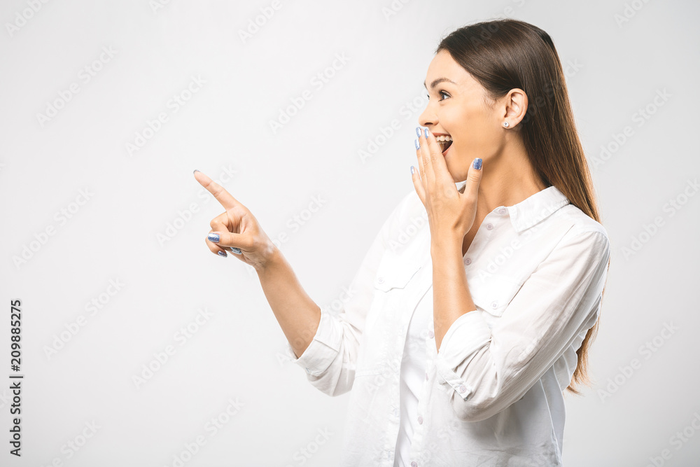 Wall mural Young beautiful smiling woman presenting your product, isolated over white background. Place for text. Surprised woman looking sideways in excitement. Isolated over white background