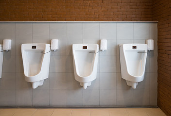 three white urinals in men toilet with automatic flushing sensor
