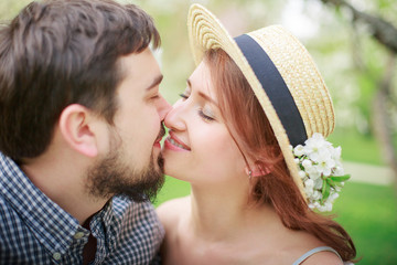 Couple in love kissing in the spring garden. Romantic valentine's day. Young beautiful girl in a straw hat with a flower