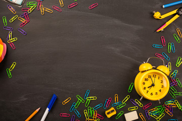 bright office supplies, yellow alarm clock on black chalkboard top view, copy space. concept: back to school, school's out, school holidays, teacher's day