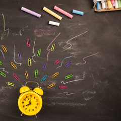 yellow alarm clock, chalk and clips on black chalkboard top view. concept: back to school, school holidays, time to get up Wake up to college