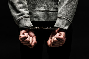 Close-up of a man's hands handcuffed. The concept of violence. On black background