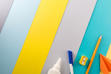 school and office supplies on bright striped background. minimum set in yellow, blue, gray and orange color: pen, pencil, sharpener, glue. concept: back to school, minimalism. Flat lay, top view