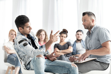 Mixed-race teenager talking to a school counselor in detention. Blurred classmates in the background