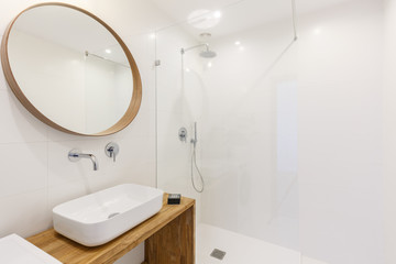 Mirror above washbasin in white bathroom interior with lights and shower. Real photo