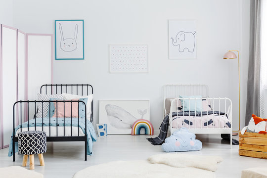 Minimal bedroom interior for two children. Metal frame beds, some toys and posters of a rabbit, an elephant and a whale on a white wall. Real photo