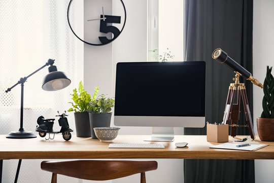 Lamp and computer desktop on wooden desk in modern freelancer's interior with clock. Real photo