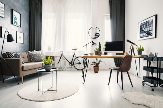Black chair at wooden desk with computer desktop in workspace interior with sofa and bike. Real photo