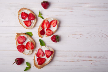 Toasts or bruschetta with strawberries on cream cheese on white wooden background. Top view. Copy space