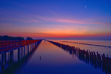 Fishermen leave fishing while the twilight is on and the crescent moon still shines at wooden red bridge over the sea.