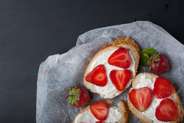 Toasts or bruschetta with strawberries on cream cheese on black background. Top view. Copy space