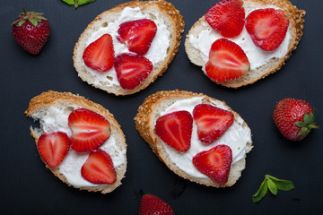 Toasts or bruschetta with strawberries on cream cheese on black background. Top view. Copy space