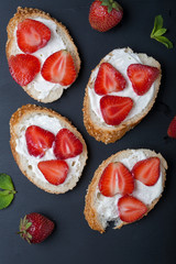 Toasts or bruschetta with strawberries on cream cheese on black background. Top view. Copy space
